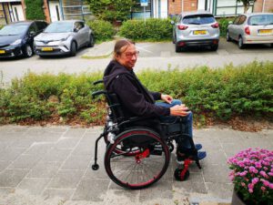 Foto van Peter in een rolstoel op de stoep van de Eikenstraat.